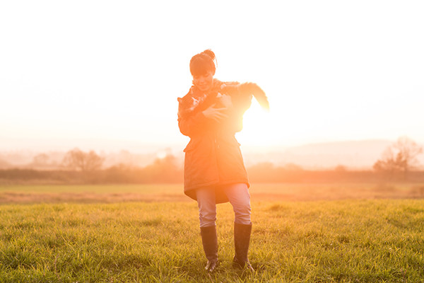 A woman standing in a field holds her Norwegian Forest Cat.